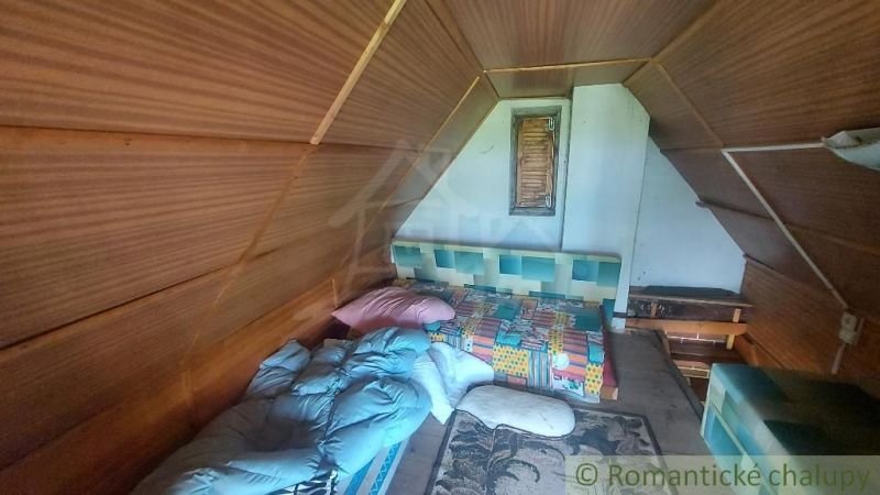 Interior of a cabin with wooden wall decor, a bed, and colorful blankets.