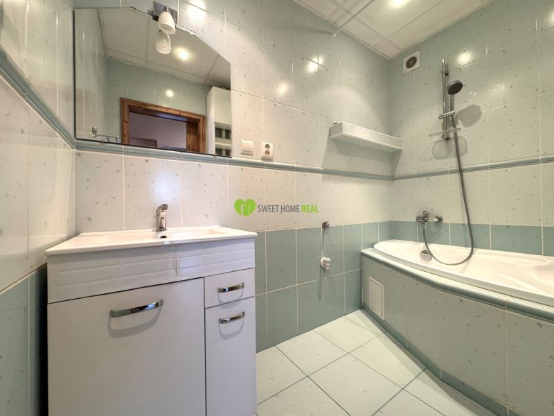 A bathroom with light tiles and a hanging bathtub in a 3-room apartment.