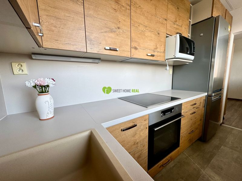 A kitchen in a 3-room apartment with a wood-patterned floor and modern appliances.