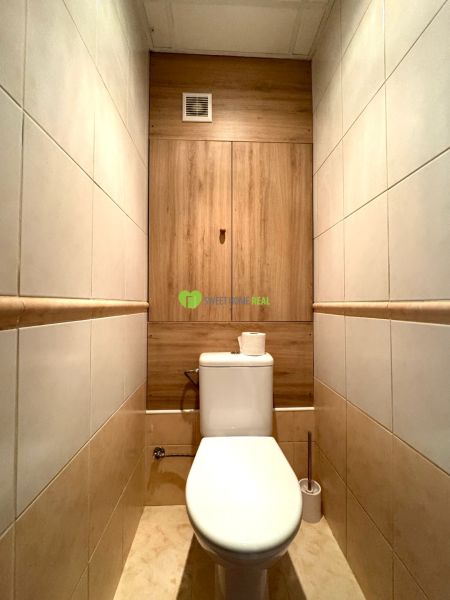 Bathroom in a 3-room apartment with tiles and a toilet, wooden decor on the wall.