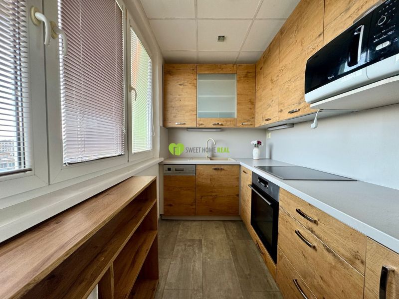 A kitchen in a 3-room apartment with a kitchen unit, wooden decor flooring, and large windows.