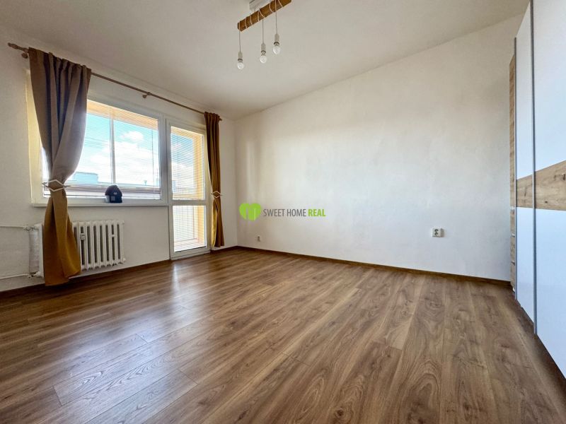 A room in a three-room apartment with a wood-decorated floor and a large window.