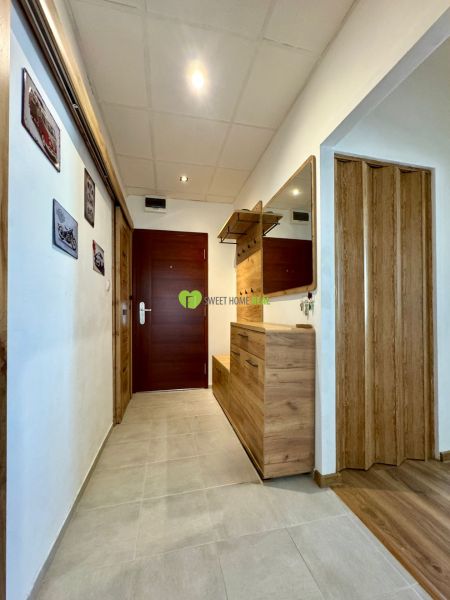 A hallway in a 3-room apartment with a tiled floor, a mirror, and wooden decor.