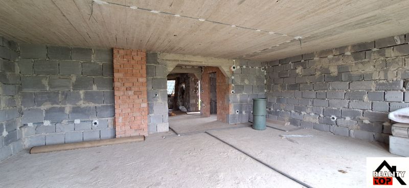 An incomplete wall in a family house made of bricks and concrete, without flooring finishes.