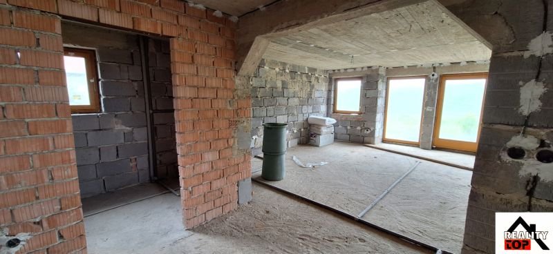 An unfinished interior of a family house with unplastered brick walls and large windows.