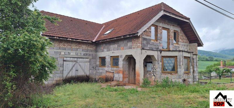 A family house in Stará Bašta made of gray brick with a red roof and wooden doors.
