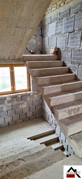 A staircase in an unfinished family house with gray bricks and a wooden window.