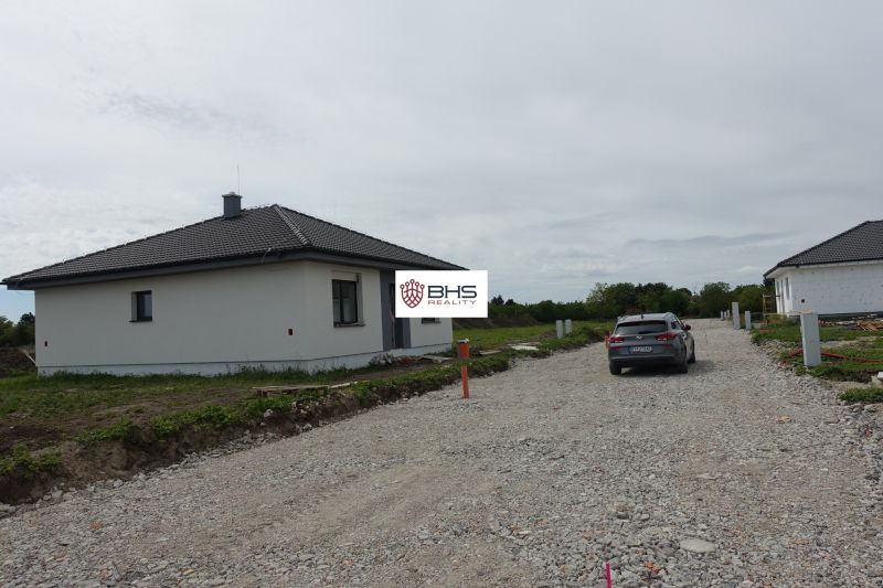 A family house in Reca with a car on a gravel access road and a garden.