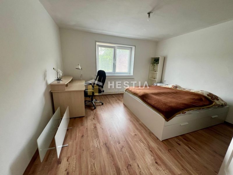 A room in a family house with a bed, a desk, and a wooden-decor floor.