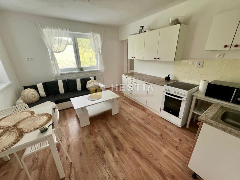 A kitchen in a family house with a wooden decor floor, white furniture, and a sofa.