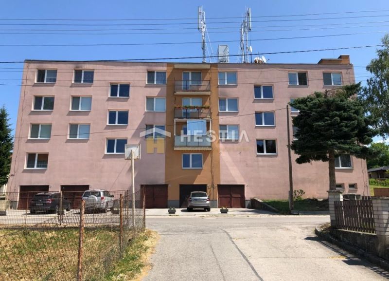 Brick building in Moravské Lieskové, a place for a 3-room apartment, surroundings with cars and trees.