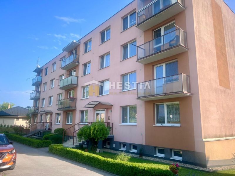 A four-story apartment building in Moravské Lieskové with a parking lot and maintained greenery.