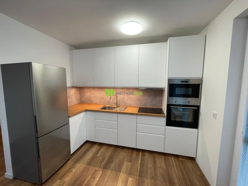 A kitchen in a 2-room apartment with a white kitchen unit and a floor with a wood decor.
