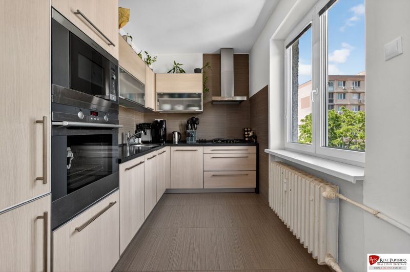 A kitchen with corner cabinets, built-in appliances, and a large window in a 3-room apartment.