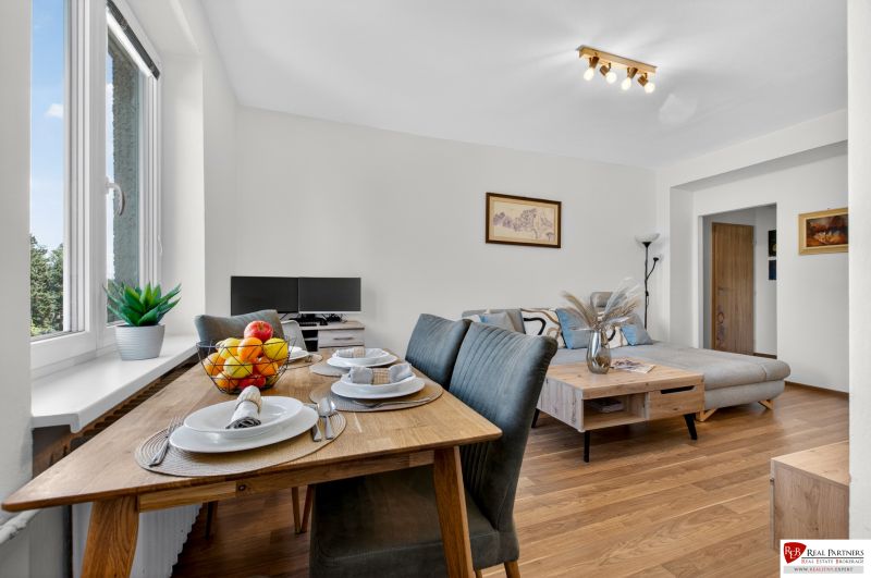 Dining room with a wooden table and a living room in a 3-room apartment with a wooden decor floor.