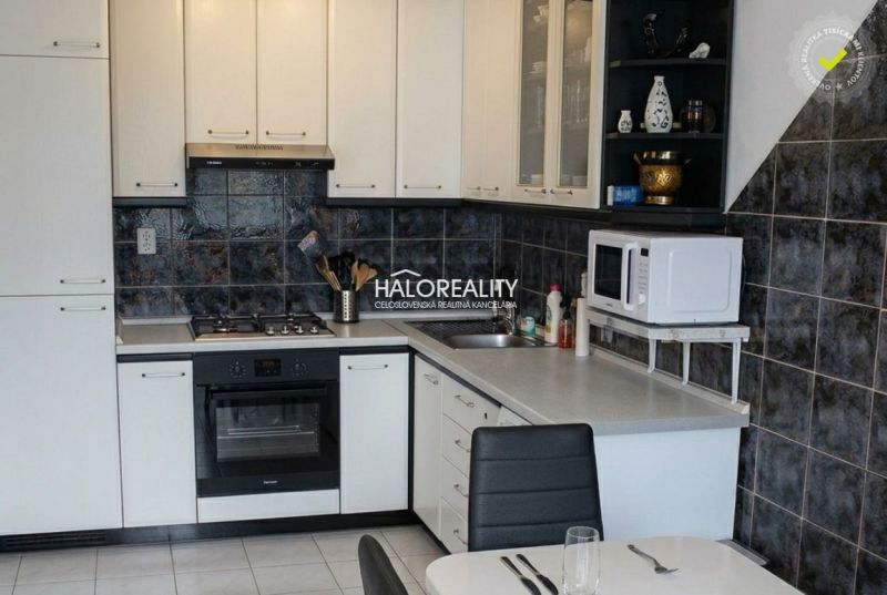A kitchen unit with white cabinets and dark tiled backsplash in a 3-room apartment.