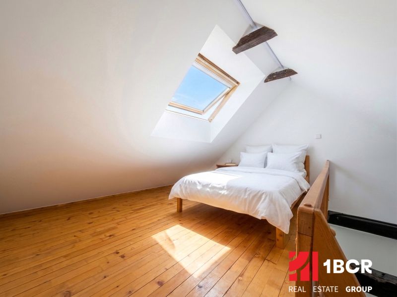 Attic bedroom with a bed and a skylight, wooden decor flooring.