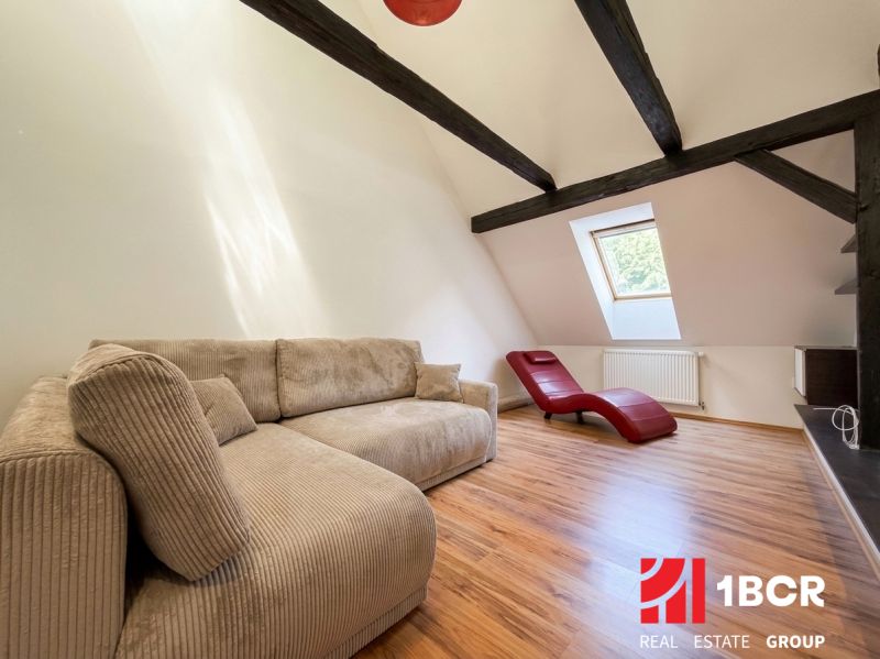 A room in a 2-room apartment with a beige sofa, a red armchair, and a wooden decor floor.