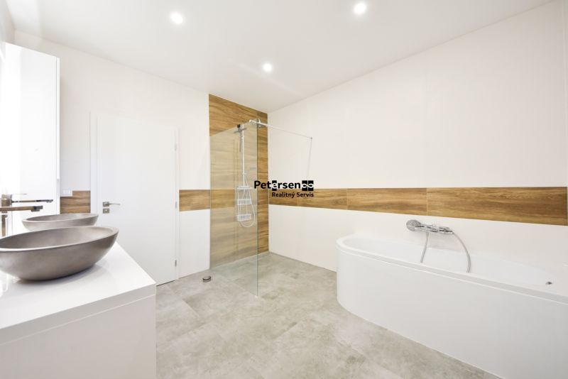 A bathroom in a family house with a bathtub, a shower, and a floor with a wooden decor.