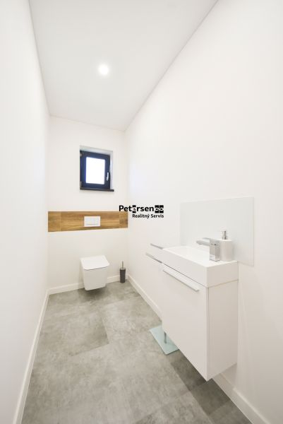 Simple toilet with a narrow sink, window, and wood-decor tiles in a family house.