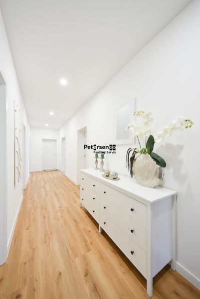 A hallway in a family house with white furniture and a wooden-patterned floor.