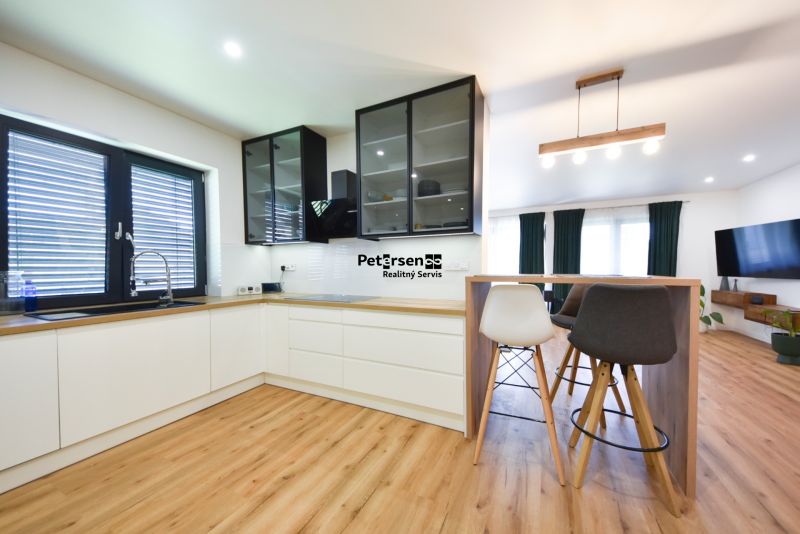 A kitchen in a family house with white cabinets, a bar counter, and a wooden decor floor.