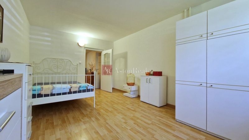 A bedroom in a 2-room apartment with white furniture and a wood-patterned floor.