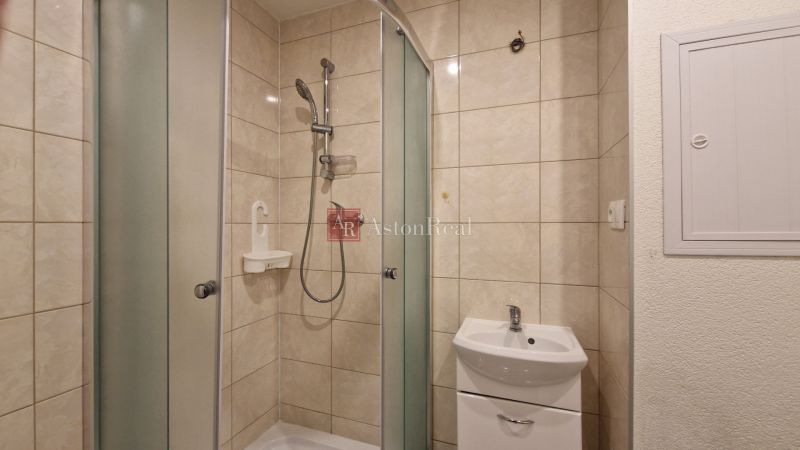 A bathroom with a shower and a sink in a 2-room apartment, tiled walls.