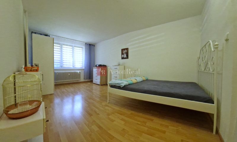 A bedroom with light, a bed, and a wooden decor floor in a two-room apartment.