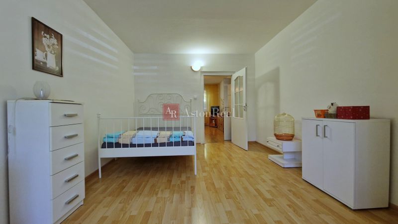 Bedroom in a 2-room apartment with wood-patterned flooring, a white bed, and a dresser.
