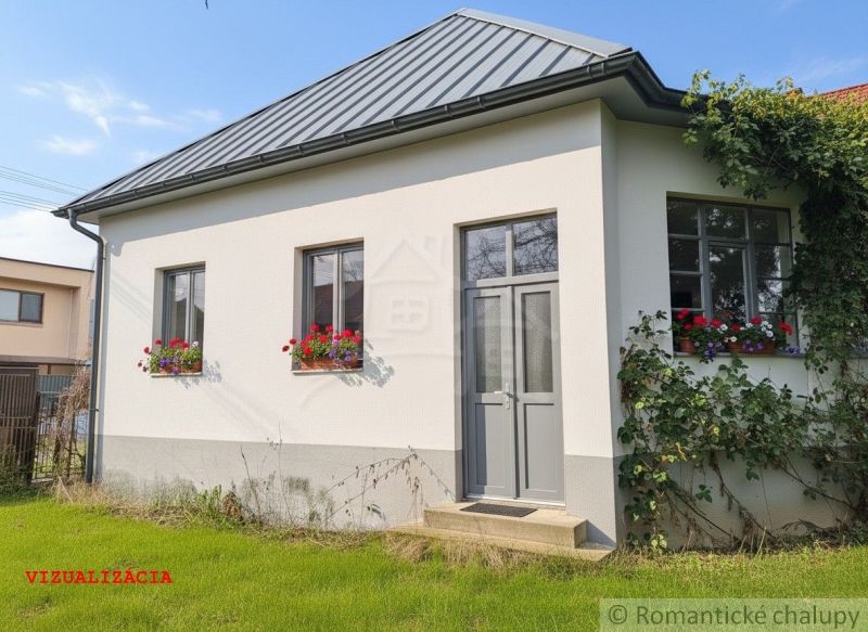 The white facade of the cottage in Divín with flowers in the windows and a green lawn.
