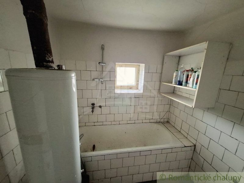 Bathroom in a cottage with tiles, a bathtub, and shelves for toiletries.
