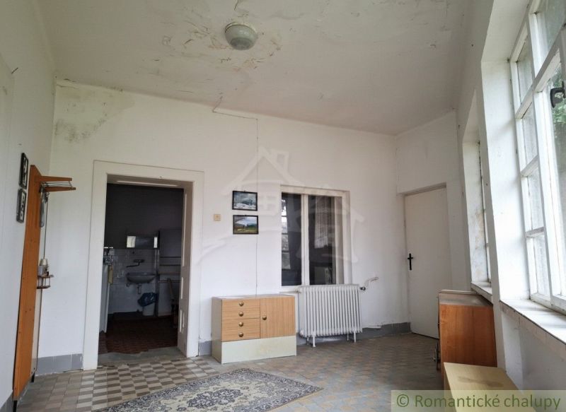 The interior of a cabin with worn walls, older furniture, and a radiator under the window.