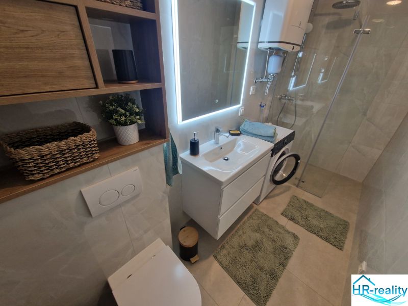 A bathroom with a sink, shower, and washing machine in a 3-room apartment.