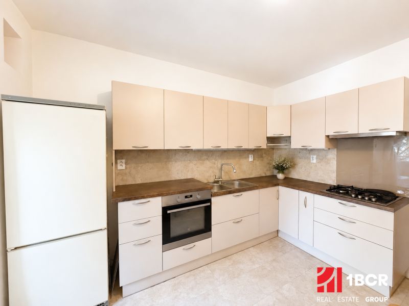 A kitchen with beige cabinets and appliances in a three-room apartment, flooring with a wood decor.