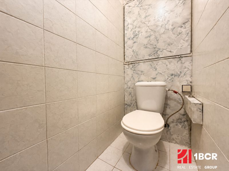 Toilet in the bathroom of a 3-room apartment with white tiles and ceramic flooring.