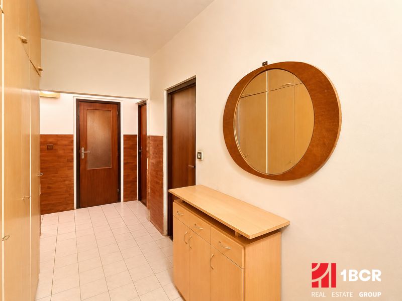 A hallway in a 3-room apartment with a round mirror and a wooden decor floor.
