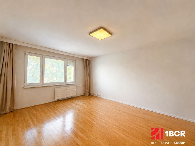 A spacious room with a wood-patterned floor in a 3-room apartment, neutral walls.