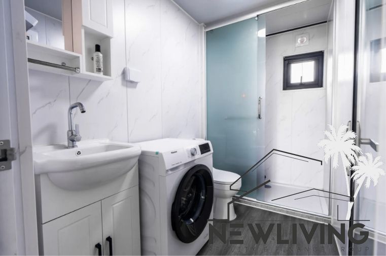 Bathroom with a washing machine in a family house, white cabinets, glass shower, and mirror.