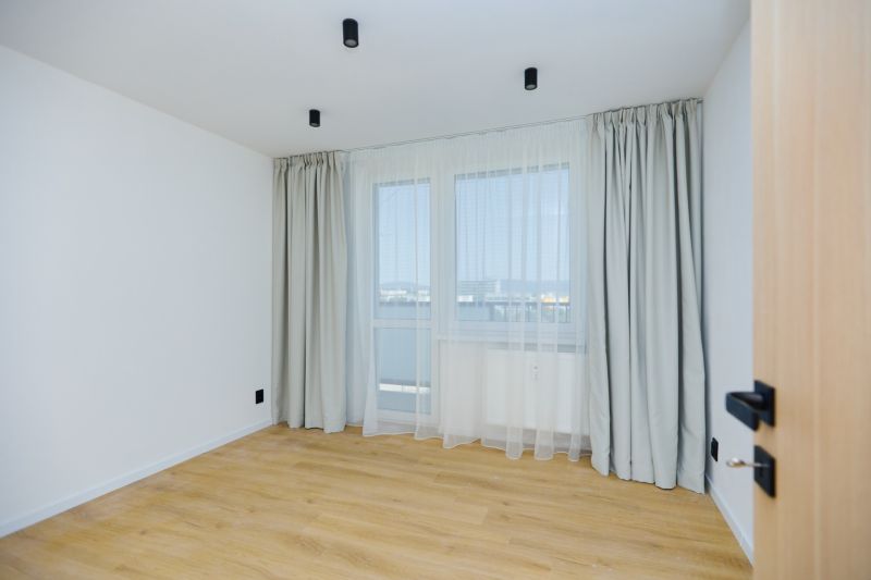 An empty room in a 4-room apartment with white walls and a wooden-patterned floor.