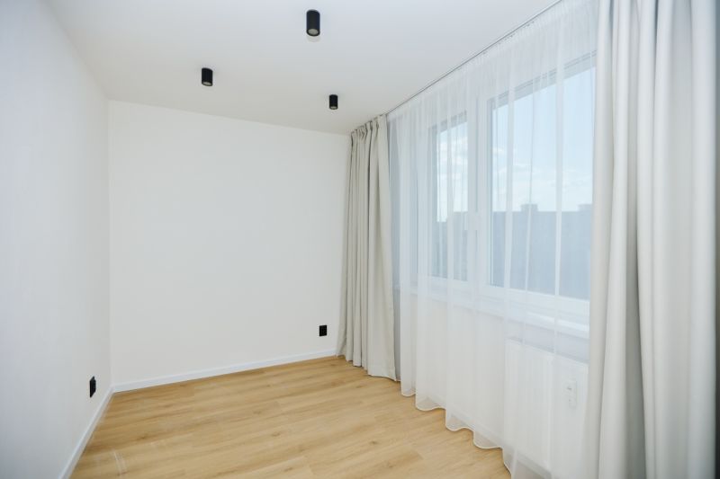 A room in a 4-room apartment with light-colored walls, a window, and a floor with a wood decor.