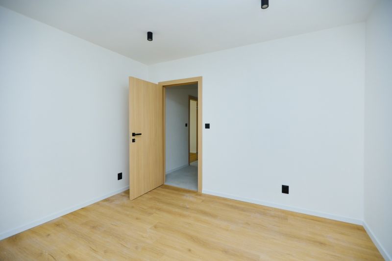 An empty room with wood-patterned flooring and open doors in a 4-room apartment.