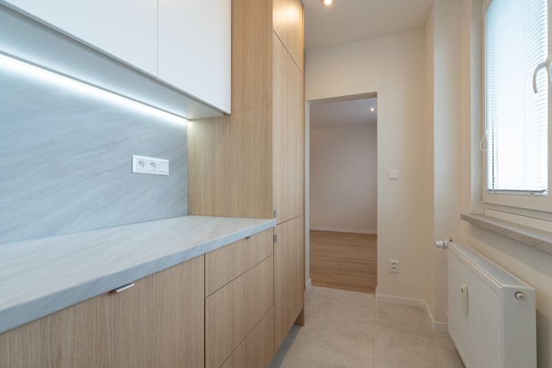 A narrow kitchen with light cabinets that frame the entrance to another room.