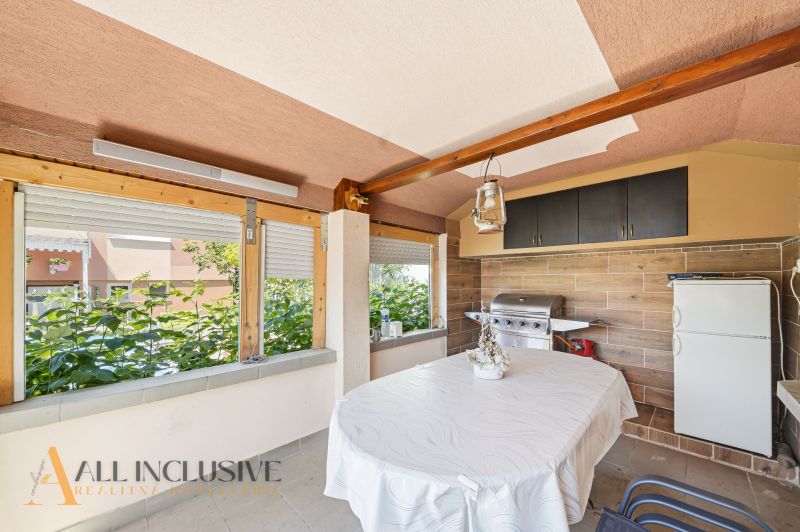 A covered terrace with a grill in a family house, surrounded by greenery.