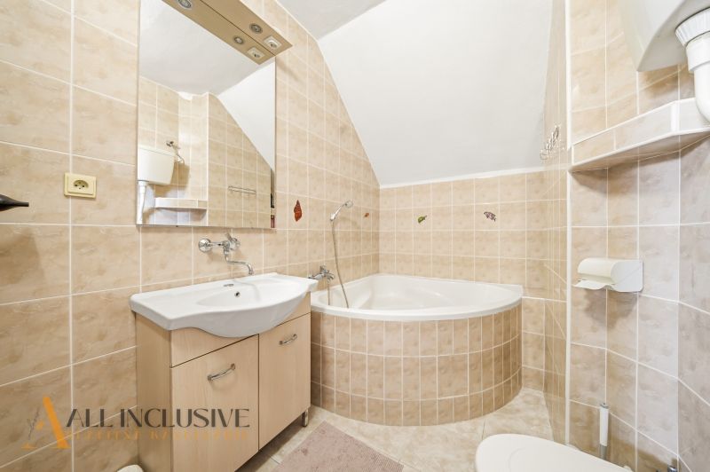 A bathroom with light tiles, a corner bathtub, and a sink in a family house.