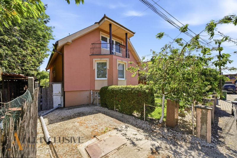 A family house in Gabčíkovo with a pink facade, a balcony, and a garden, surrounded by greenery.