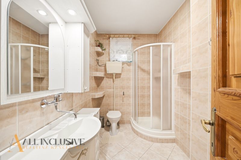 A bathroom in a family house with a sink, shower, and toilet on beige tiles.