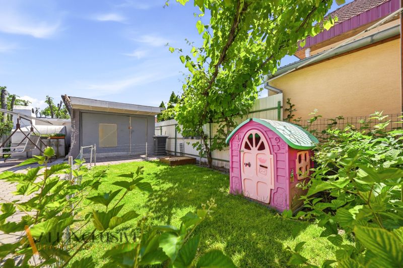 The courtyard of a family house in Gabčíkovo with a children's playhouse and a pergola, surrounded by greenery.
