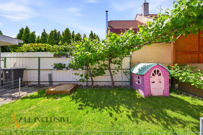 The garden of a family house in Gabčíkovo with a sandbox and a children's playhouse on the grass.
