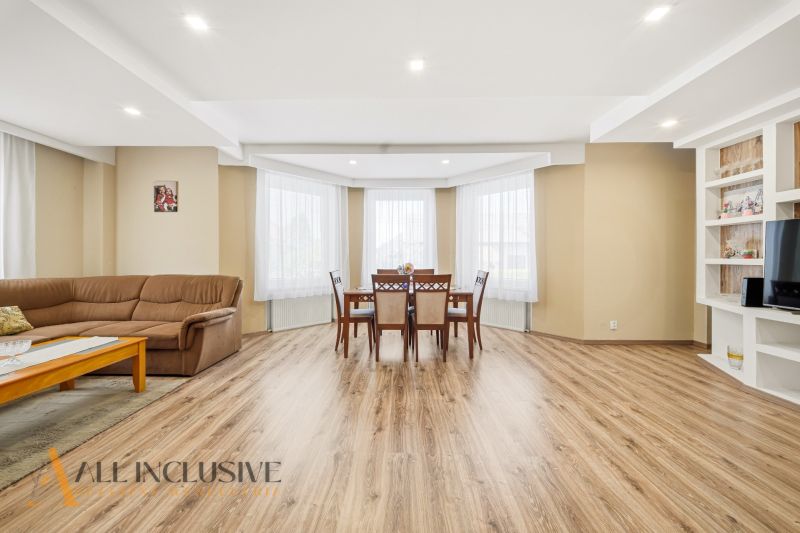 Living room with a sofa, dining table, and wood-patterned flooring in a family house.